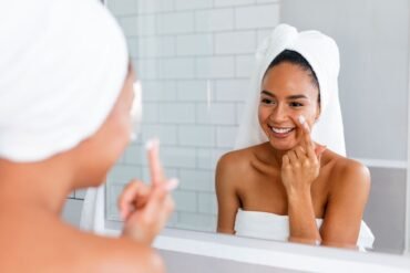 Mujer aplicándose crema hidratante en el espejo